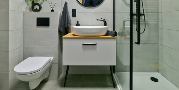 A sleek, modern small bathroom featuring a bright walk-in shower with clear glass doors, light wall panels, and smart built-in 